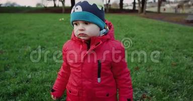 小可爱穿着红色夹克和滑稽的帽子走在中央公园的绿草上。 红色史诗4k。 慢动作。